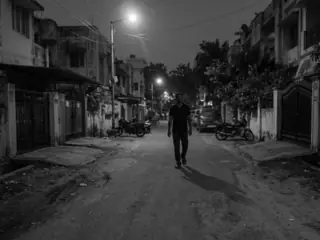 A black-and-white 320 by 240 frame from the watch: a man walking up a dark street, a few metres away - a person, too small to identify